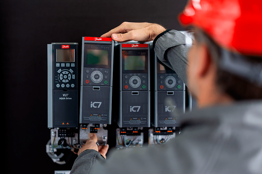 Profesional realizando una revisión técnica de variadores Danfoss iC7-Automation y VLT AQUA Drive instalados en un cuadro eléctrico.